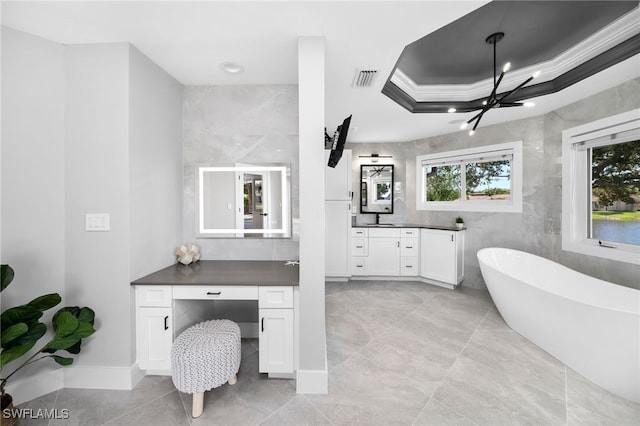 bathroom with a bathtub, ornamental molding, vanity, a tray ceiling, and a notable chandelier