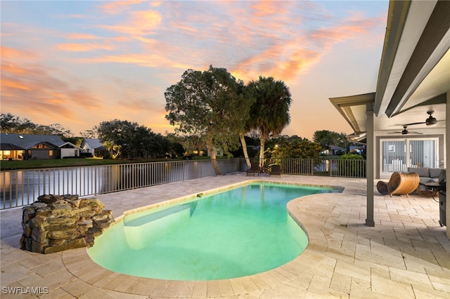 pool at dusk featuring ceiling fan and a patio area