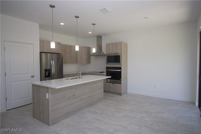 kitchen with sink, wall chimney exhaust hood, an island with sink, decorative light fixtures, and appliances with stainless steel finishes