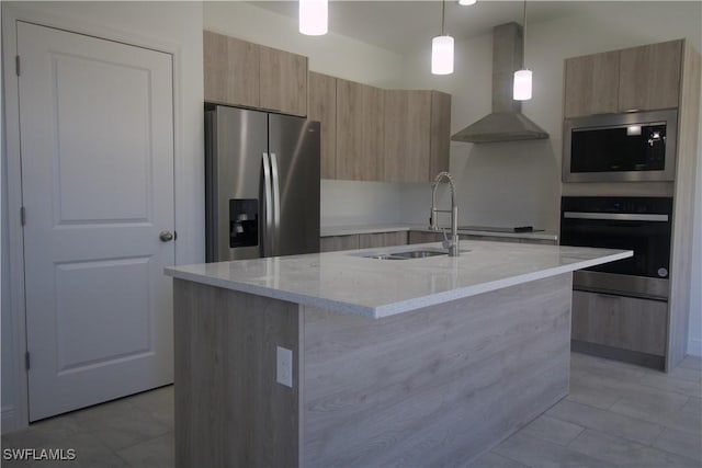 kitchen featuring light stone countertops, wall chimney range hood, an island with sink, decorative light fixtures, and appliances with stainless steel finishes