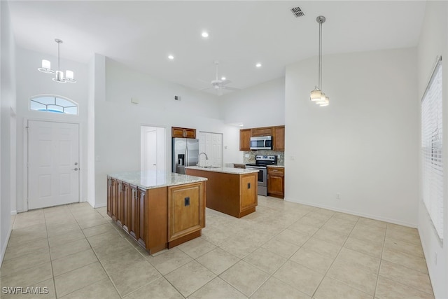 kitchen with a center island, a towering ceiling, stainless steel appliances, and hanging light fixtures