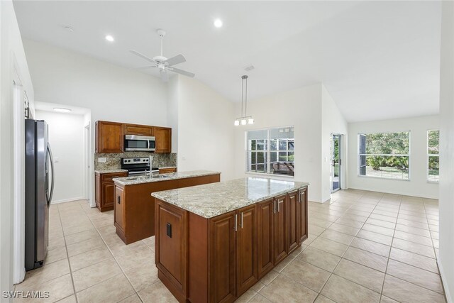 kitchen featuring appliances with stainless steel finishes, backsplash, light stone counters, a center island, and hanging light fixtures