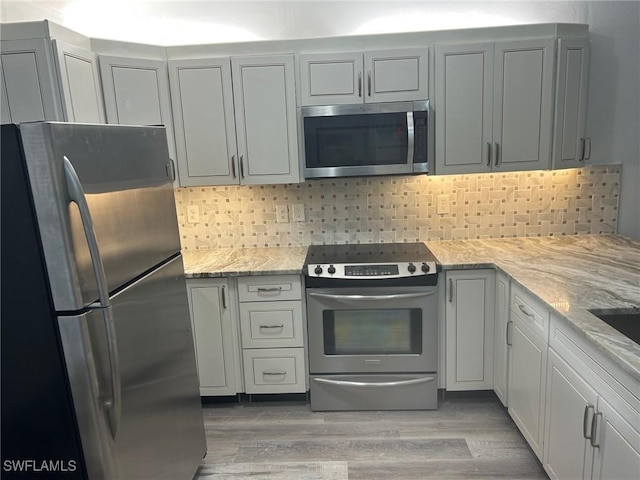 kitchen with decorative backsplash, light stone counters, light wood-type flooring, and stainless steel appliances