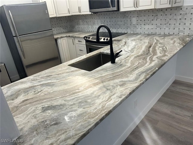 kitchen featuring hardwood / wood-style flooring, white cabinets, light stone countertops, and appliances with stainless steel finishes