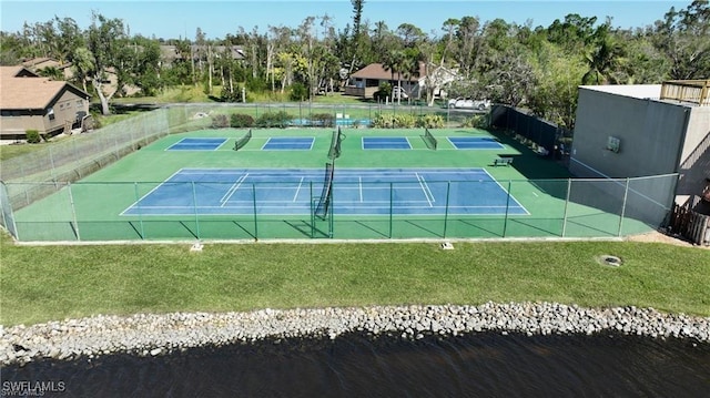 view of sport court with a water view and a lawn