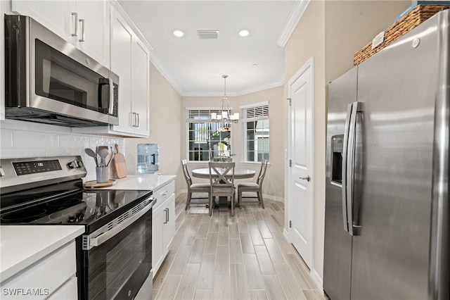 kitchen with stainless steel appliances, crown molding, a chandelier, white cabinetry, and hanging light fixtures