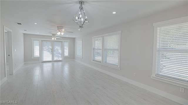 unfurnished room featuring ceiling fan with notable chandelier and light wood-type flooring