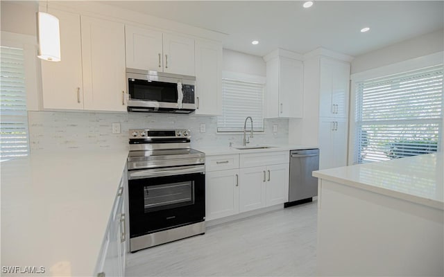 kitchen featuring pendant lighting, light countertops, appliances with stainless steel finishes, white cabinets, and a sink