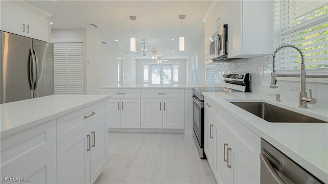 kitchen featuring stainless steel appliances, a sink, white cabinets, light countertops, and decorative light fixtures