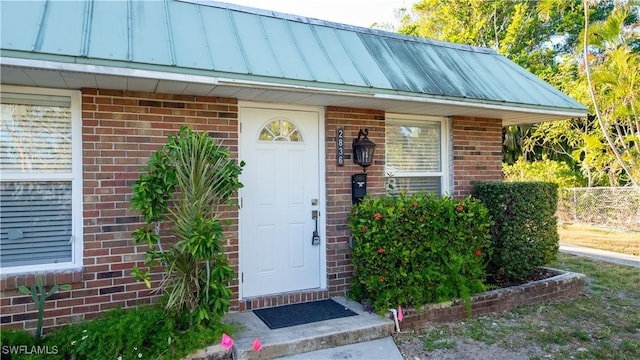 entrance to property featuring metal roof, brick siding, a standing seam roof, and fence