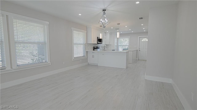 kitchen with stainless steel appliances, light countertops, hanging light fixtures, white cabinetry, and a peninsula