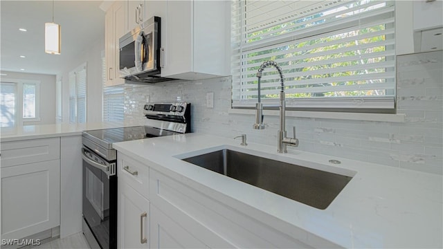 kitchen featuring a sink, white cabinetry, hanging light fixtures, appliances with stainless steel finishes, and tasteful backsplash