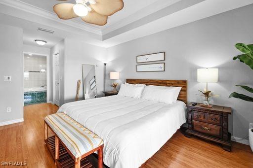 bedroom with ensuite bath, ceiling fan, hardwood / wood-style floors, a tray ceiling, and ornamental molding