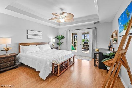 bedroom with ceiling fan, french doors, a tray ceiling, wood-type flooring, and access to outside