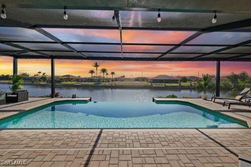 pool at dusk featuring a lanai, a water view, and a patio