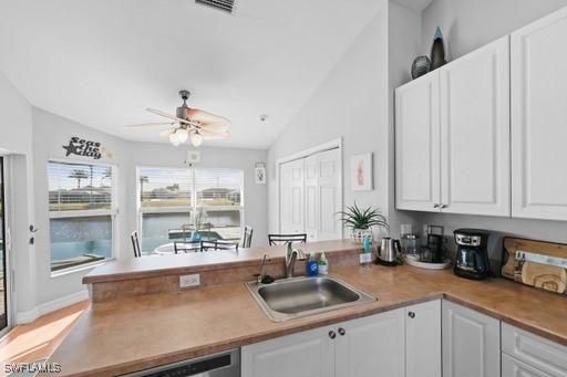 kitchen with stainless steel dishwasher, ceiling fan, sink, white cabinetry, and lofted ceiling