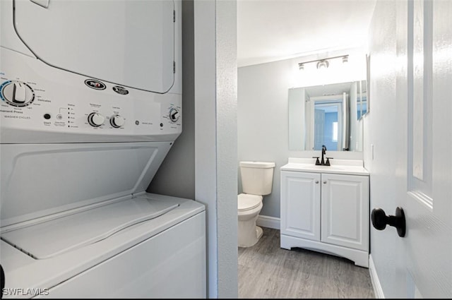 bathroom featuring vanity, hardwood / wood-style flooring, toilet, and stacked washer / dryer