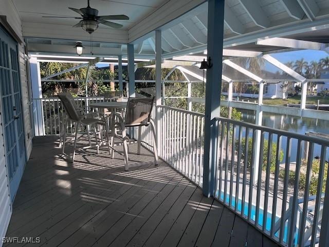 wooden deck featuring a water view, glass enclosure, and ceiling fan