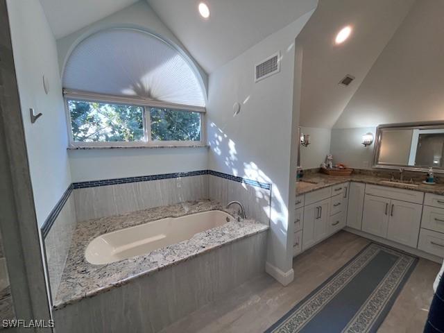 bathroom with vanity, vaulted ceiling, and a bathtub