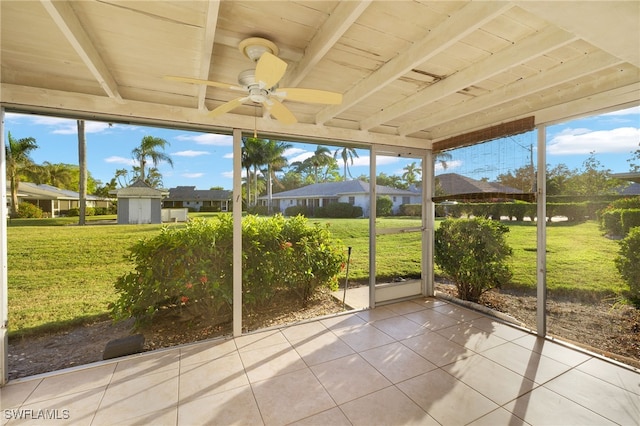 unfurnished sunroom featuring beam ceiling, ceiling fan, plenty of natural light, and wooden ceiling