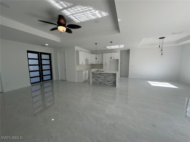 unfurnished living room featuring a tray ceiling, ceiling fan, sink, and french doors