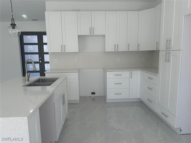 kitchen with light stone countertops, tasteful backsplash, sink, white cabinets, and hanging light fixtures