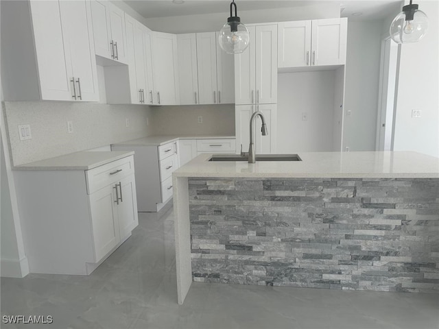 kitchen with backsplash, sink, a center island with sink, white cabinets, and hanging light fixtures