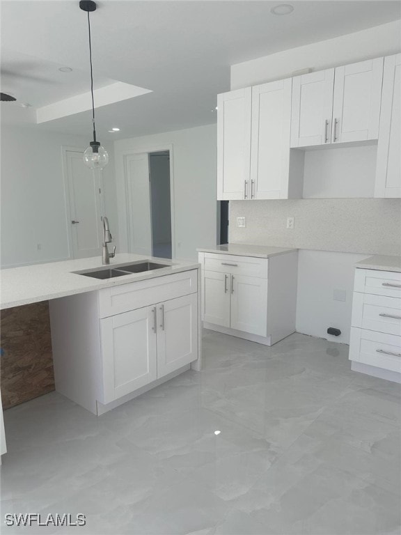 kitchen with backsplash, white cabinetry, sink, and hanging light fixtures