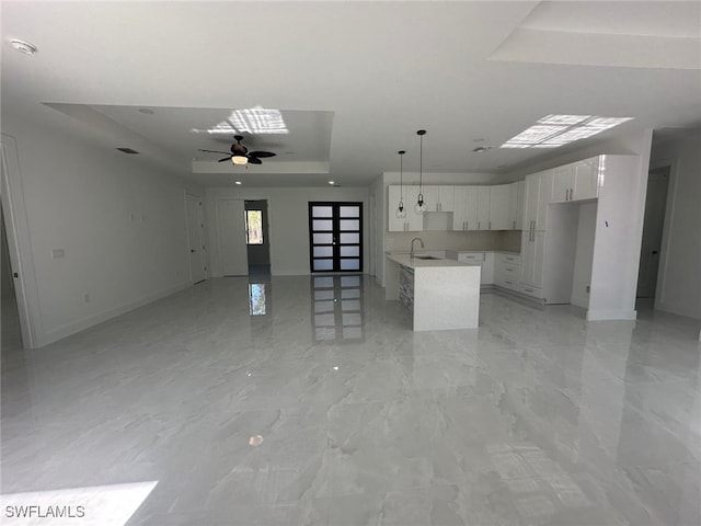 kitchen featuring a tray ceiling, ceiling fan, white cabinets, a center island, and hanging light fixtures