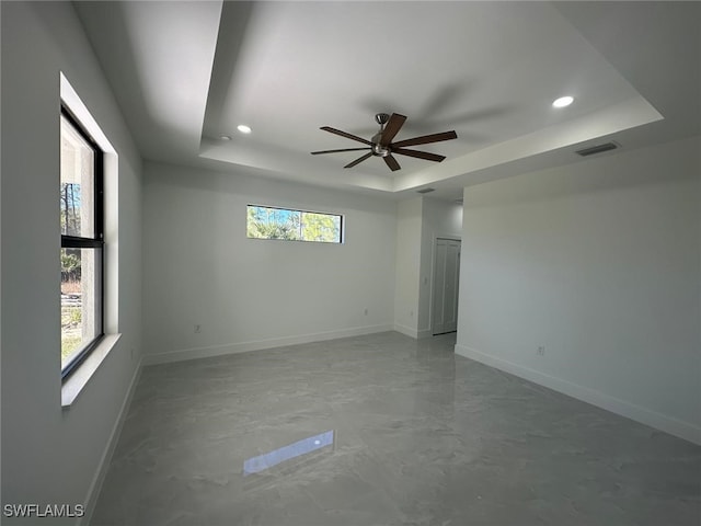 empty room with ceiling fan and a tray ceiling