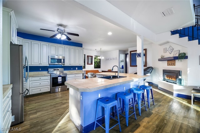 kitchen featuring dark wood-style flooring, stainless steel appliances, visible vents, a sink, and a lit fireplace