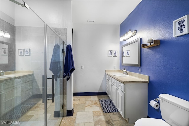 bathroom with stone tile floors, toilet, a stall shower, vanity, and baseboards