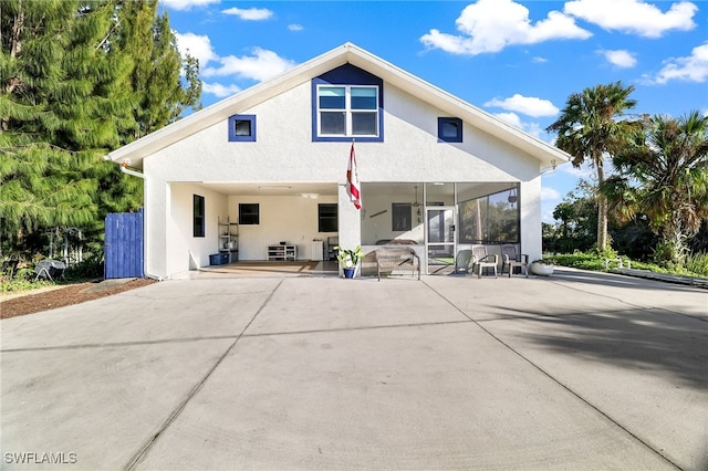 rear view of house with a sunroom, a patio area, and stucco siding