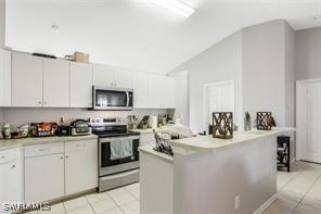 kitchen with appliances with stainless steel finishes, light tile patterned floors, white cabinetry, and lofted ceiling