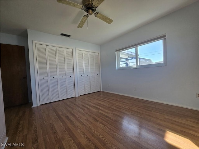 unfurnished bedroom featuring dark hardwood / wood-style floors, two closets, and ceiling fan