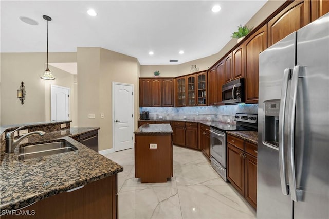 kitchen with sink, dark stone countertops, pendant lighting, stainless steel appliances, and a kitchen island with sink