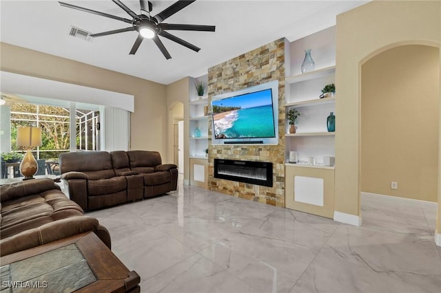 living room with a stone fireplace, built in features, and ceiling fan