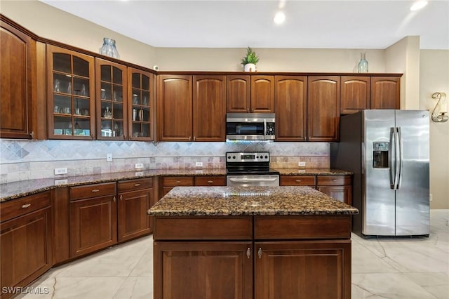 kitchen with decorative backsplash, appliances with stainless steel finishes, a kitchen island, and dark stone counters