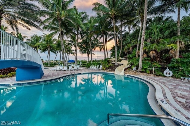 pool at dusk with a water slide and a patio