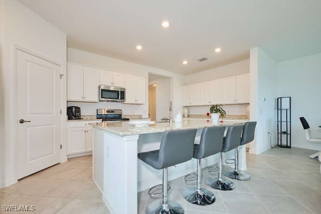 3426 Menores Way, Fort Myers, FL 33905 - kitchen with stainless steel appliances, an island with sink, white cabinetry, a breakfast bar area, and recessed lighting