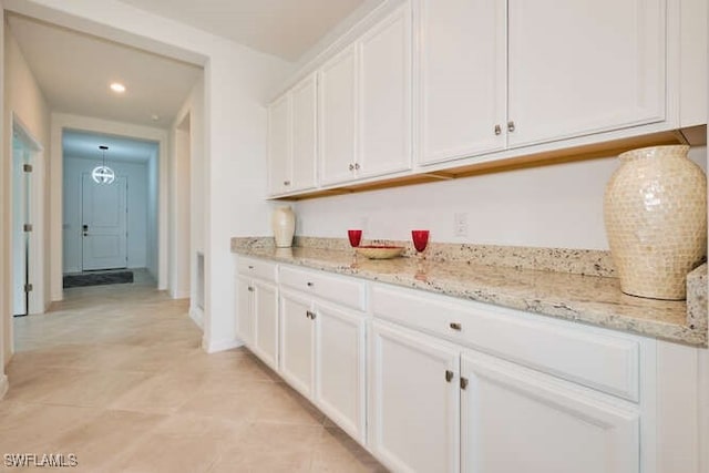 bar with white cabinets, light tile patterned floors, and light stone counters