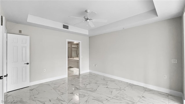 empty room with ceiling fan and a raised ceiling