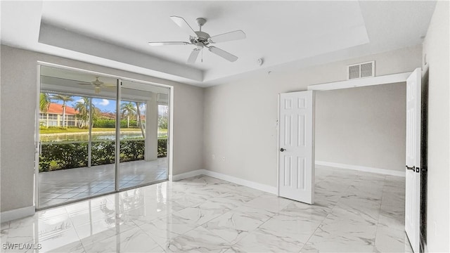 empty room featuring ceiling fan, a water view, and a tray ceiling