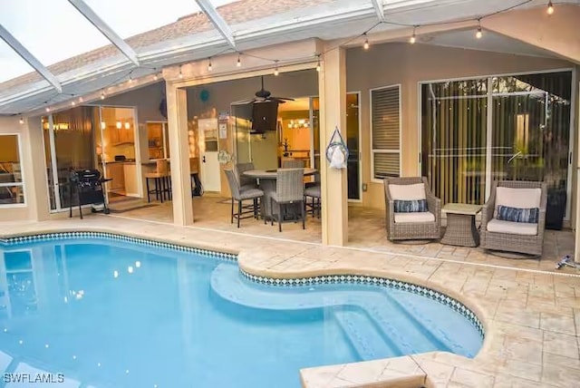 view of swimming pool with glass enclosure, ceiling fan, and a patio area