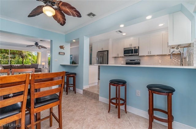 kitchen featuring decorative backsplash, appliances with stainless steel finishes, kitchen peninsula, white cabinetry, and a breakfast bar area