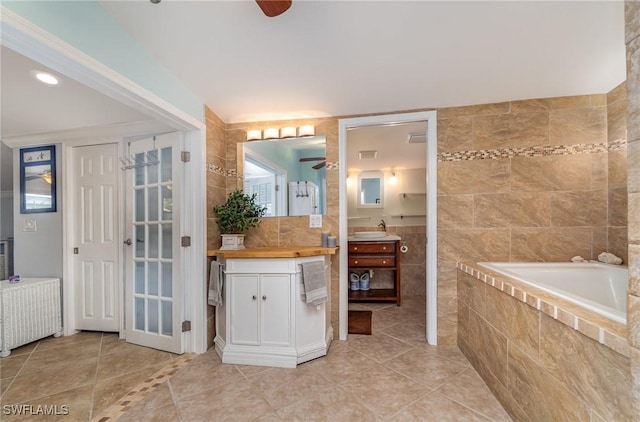 bathroom featuring vanity, tile walls, tile patterned flooring, radiator heating unit, and tiled bath