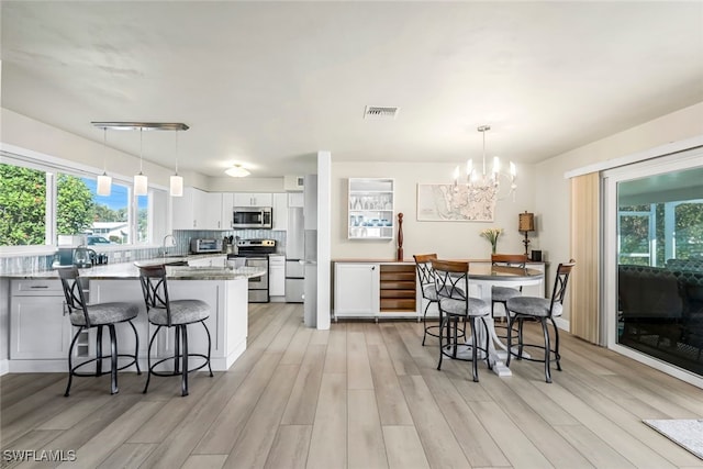 interior space featuring visible vents, light stone counters, decorative light fixtures, stainless steel appliances, and white cabinetry