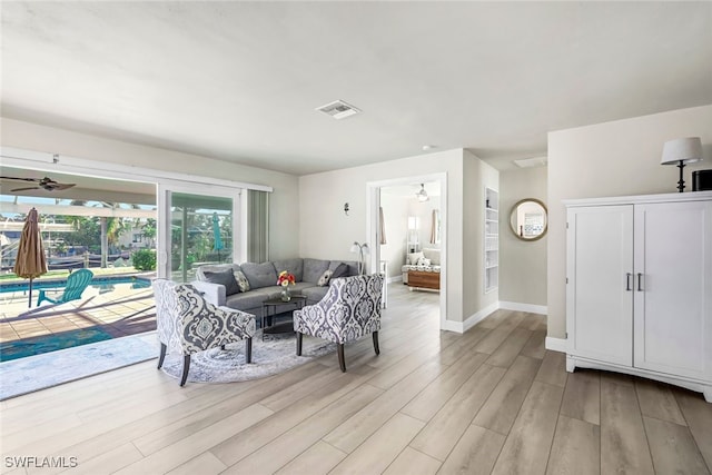 living room featuring ceiling fan, visible vents, light wood-style flooring, and baseboards