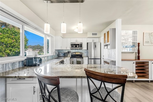 kitchen featuring white cabinetry, stainless steel appliances, decorative light fixtures, a breakfast bar, and light wood-type flooring