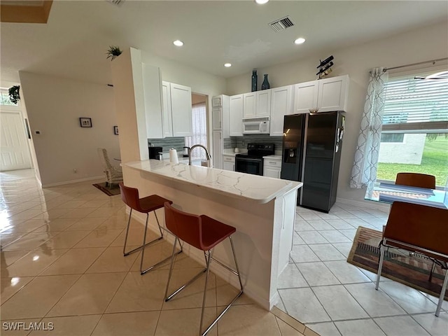 kitchen featuring kitchen peninsula, light tile patterned floors, white cabinets, and black appliances